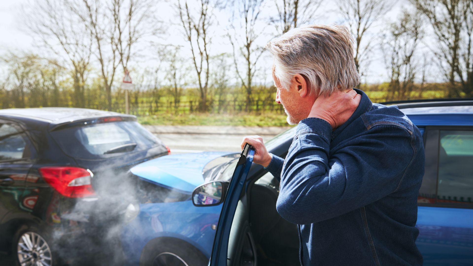 Driver holding his neck beside his car after a rear-end collision on a rural road