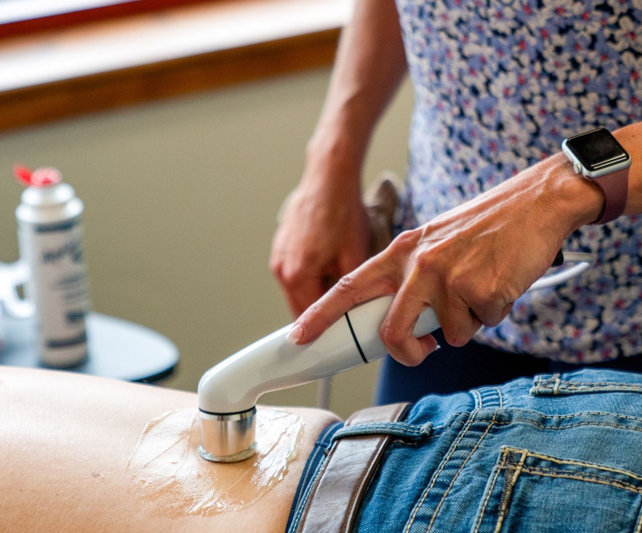 Therapeutic ultrasound applied to a patient's lower back and hip while the patient lies face down on a treatment table